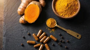 Raíz de cúrcuma fresca cortada mostrando su interior naranja intenso junto a polvo de cúrcuma y cápsulas de curcumina