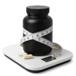 Frasco negro de suplemento, cinta métrica y cápsulas sobre báscula blanca para pérdida de peso.